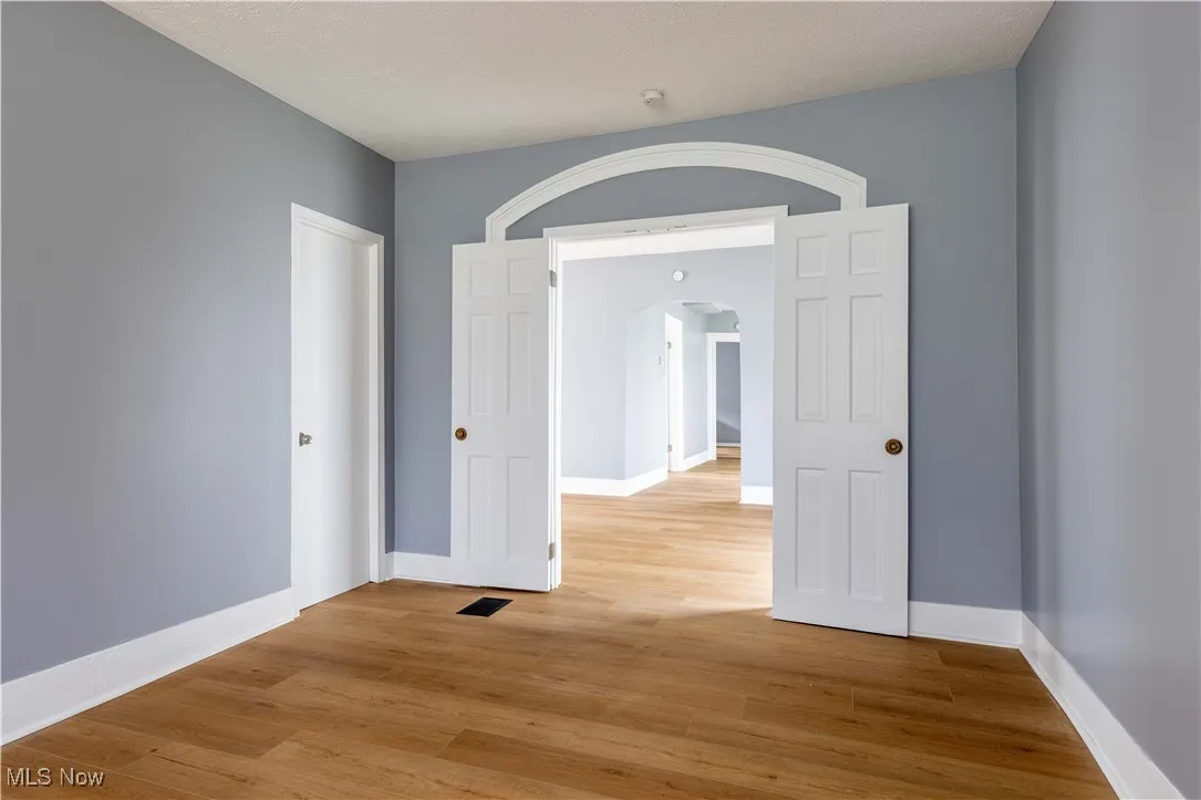 Unfurnished room with arched walkways, light wood-type flooring, and baseboards