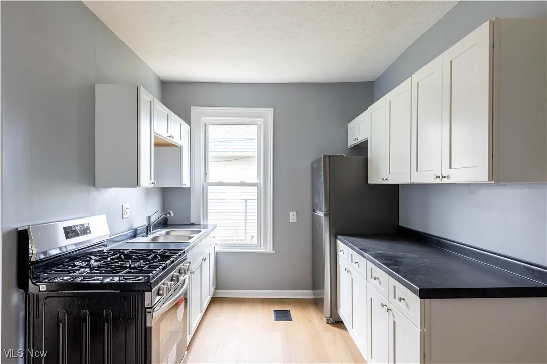 Kitchen with stainless steel appliances, a sink, light wood-style floors, white cabinets, and baseboards