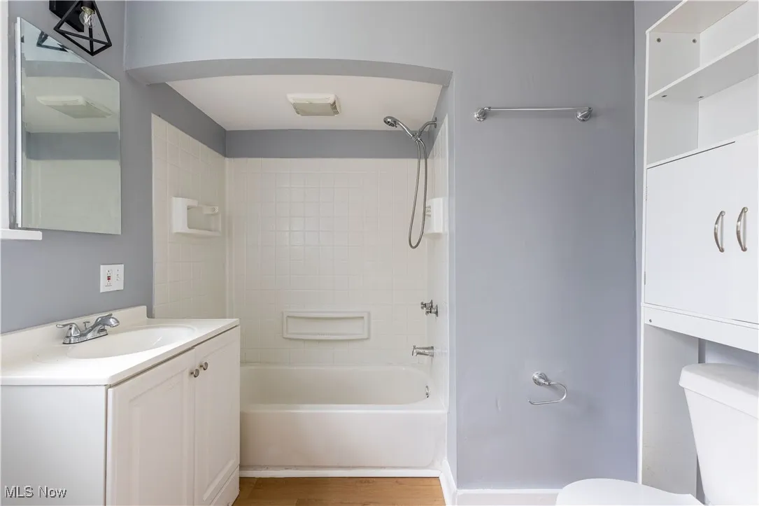 Bathroom with toilet, vanity, bathtub / shower combination, and wood finished floors