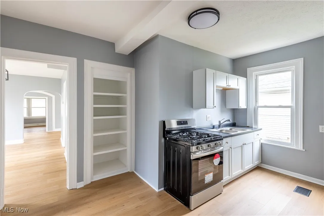 Kitchen featuring gas range, a sink, light wood-type flooring, and white cabinets