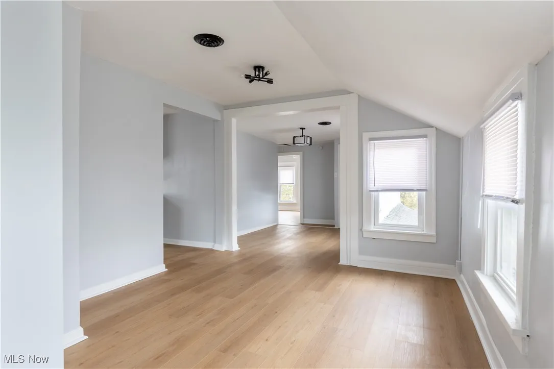 Unfurnished room with light wood finished floors, lofted ceiling, and baseboards