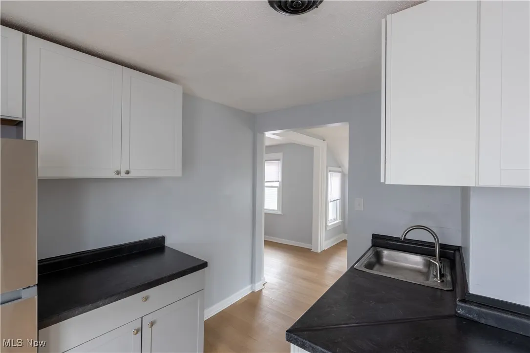 Kitchen featuring a sink, dark countertops, light wood-style floors, and white cabinetry