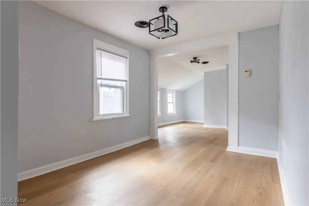 Empty room featuring light wood finished floors, baseboards, and lofted ceiling