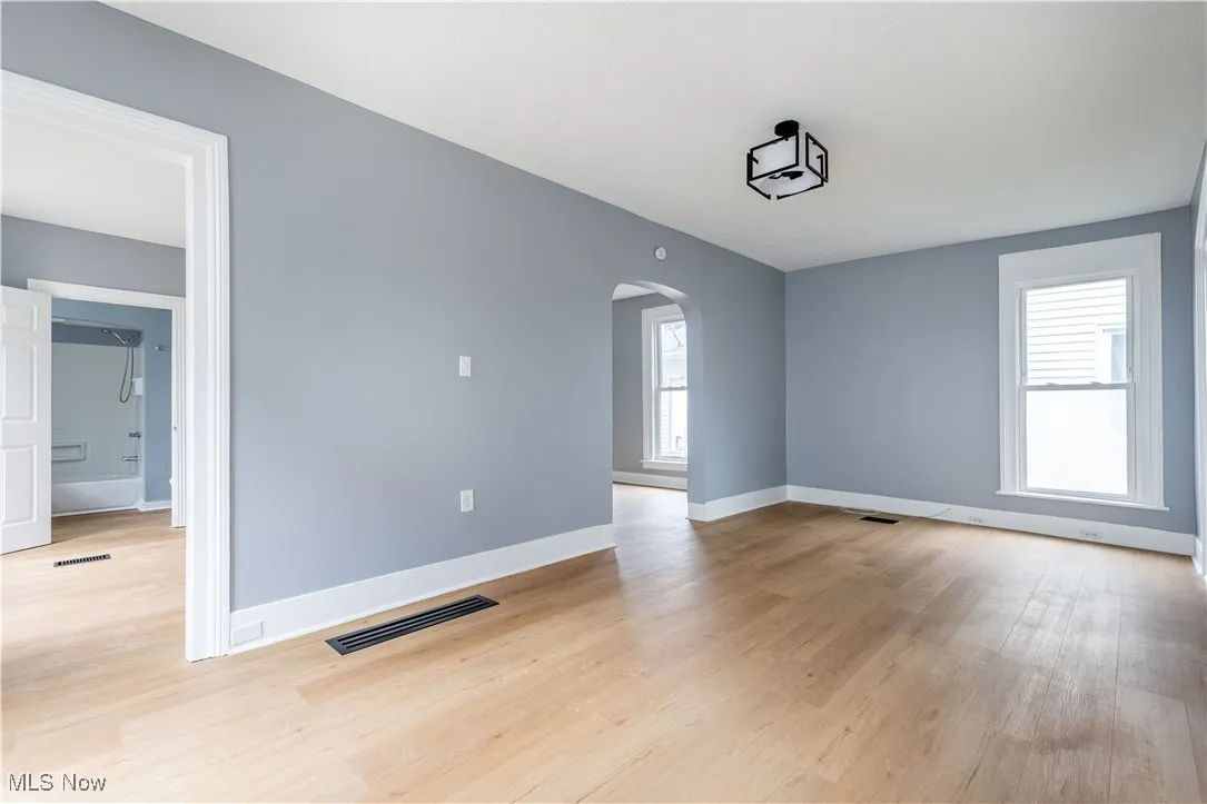 Spare room with arched walkways, light wood-type flooring, and baseboards