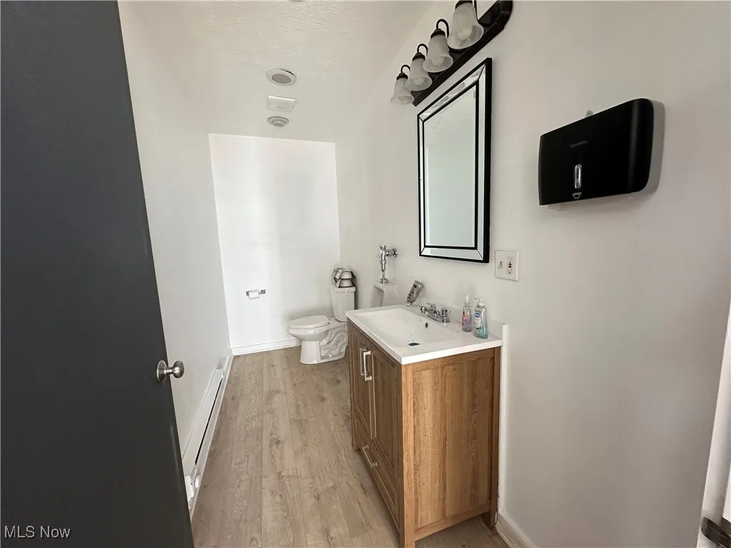 Larger building Bathroom featuring vanity, toilet, a baseboard radiator, wood finished floors, and baseboards