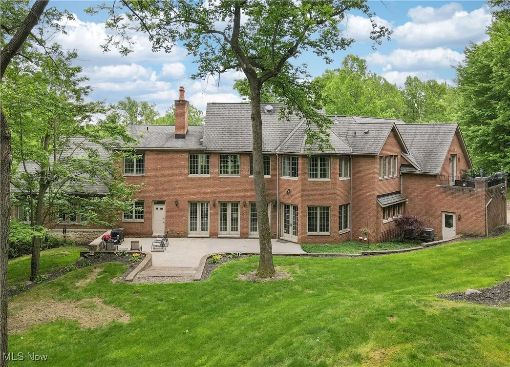 Back of property featuring a patio, brick siding, a chimney, french doors, and a lawn