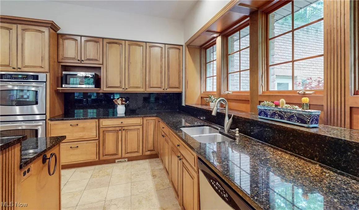 Kitchen featuring stainless steel appliances, a sink, decorative backsplash, dark stone countertops, and light tile patterned floors