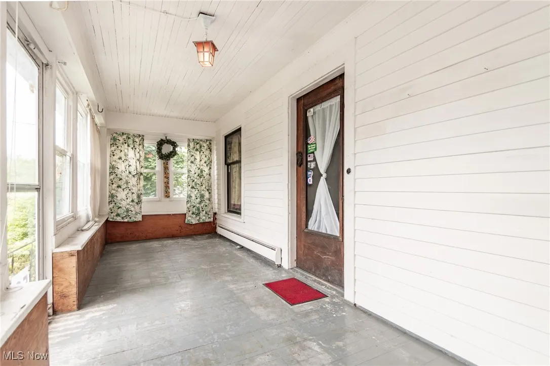 Unfurnished sunroom featuring a baseboard heating unit, wooden walls, and wood ceiling