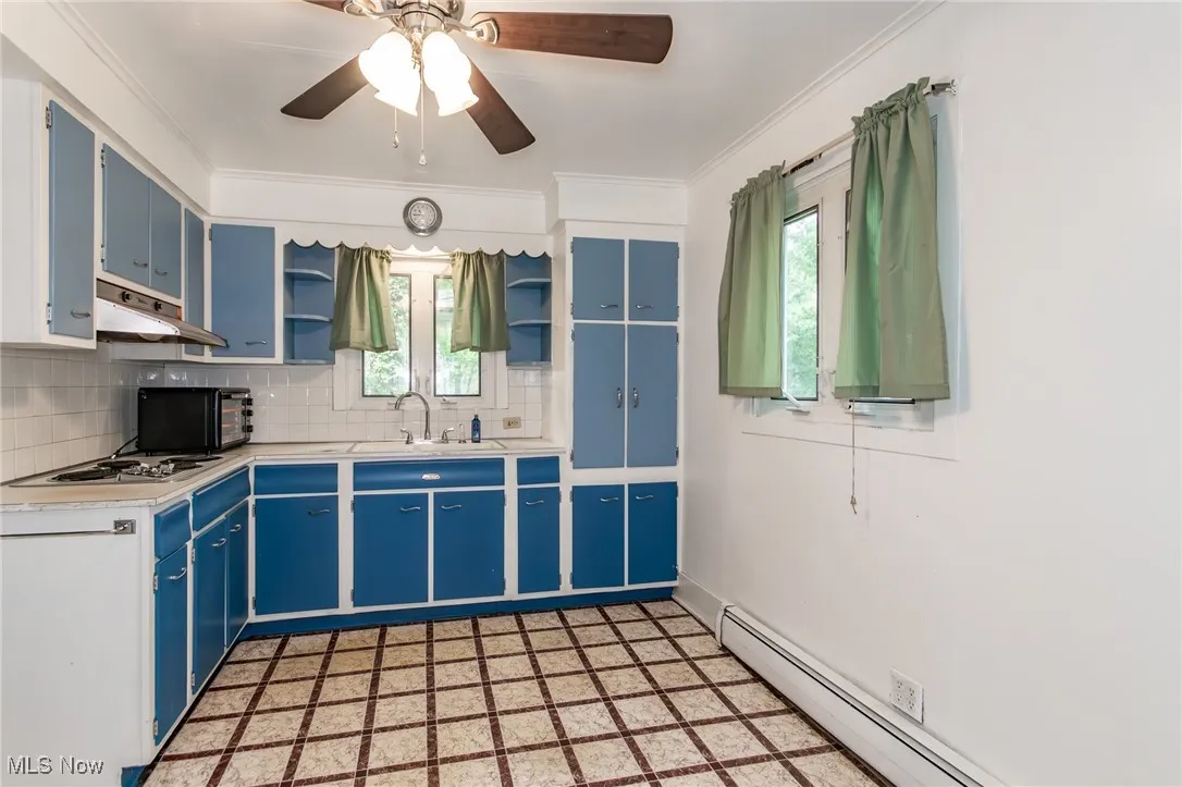 Kitchen with blue cabinets, under cabinet range hood, open shelves, baseboard heating, and a sink