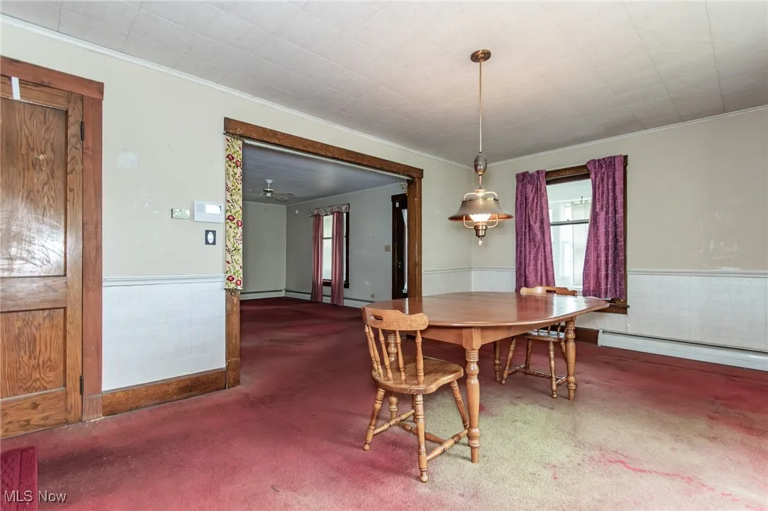 Carpeted dining room with baseboard heating, crown molding, and wainscoting