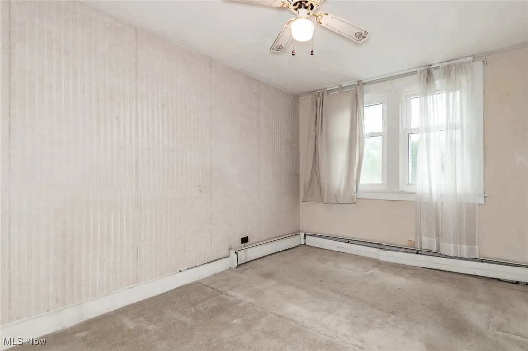 Empty room with carpet floors, a baseboard radiator, and ceiling fan