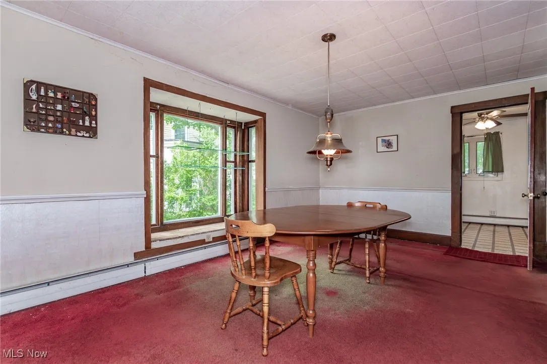 Carpeted dining room with a baseboard radiator, a wainscoted wall, crown molding, baseboard heating, and a ceiling fan