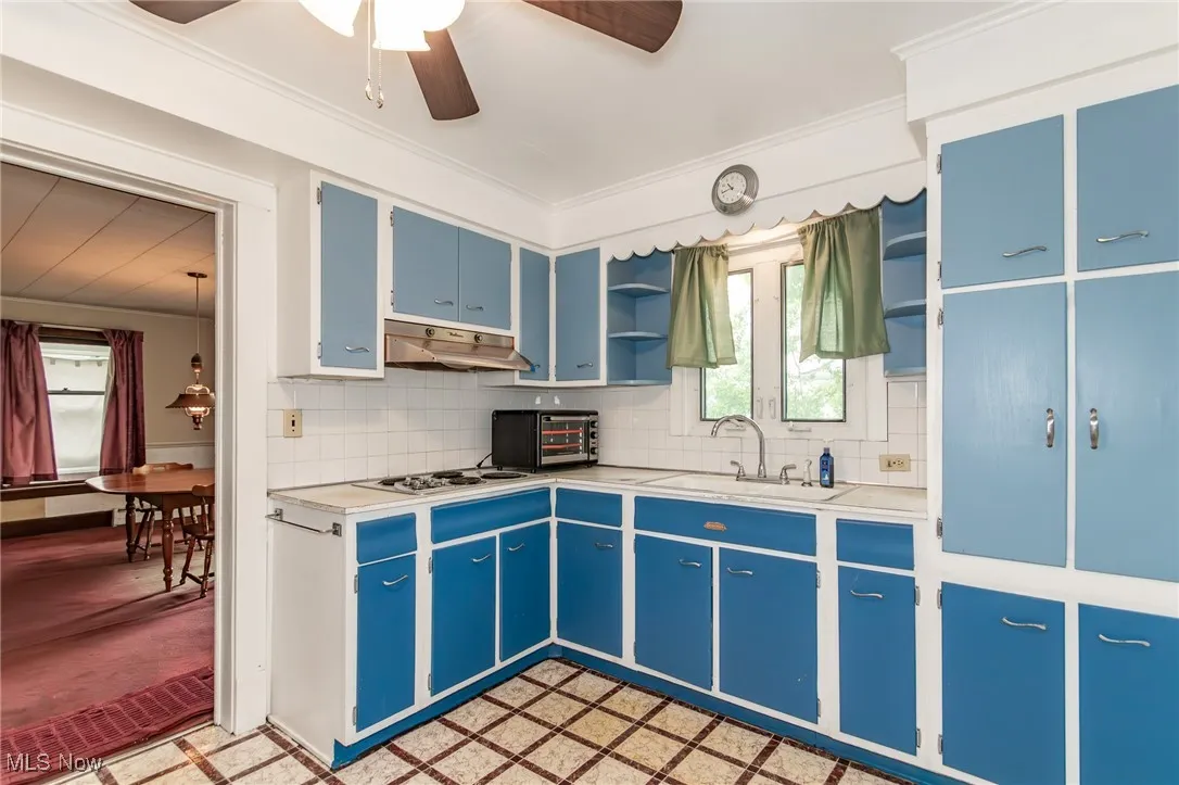 Kitchen featuring under cabinet range hood, blue cabinetry, open shelves, light countertops, and a ceiling fan