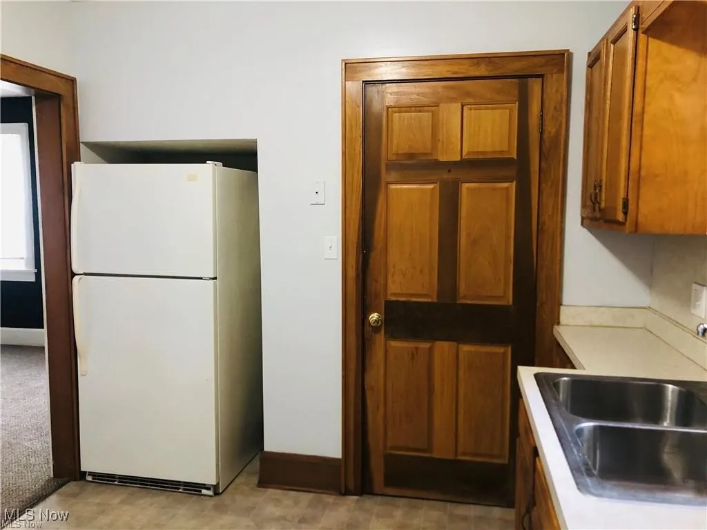 Kitchen featuring freestanding refrigerator, a sink, brown cabinetry, and light countertops
