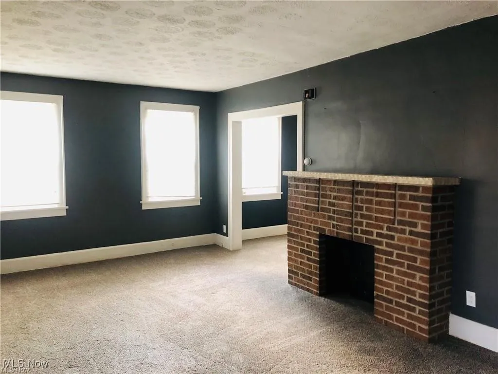 Unfurnished living room with a brick fireplace, plenty of natural light, carpet floors, and a textured ceiling