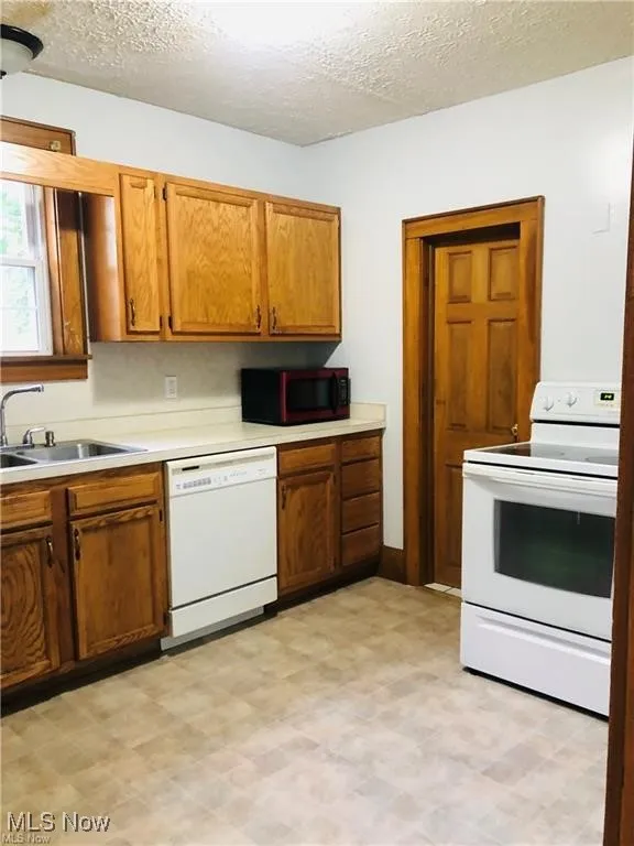 Kitchen featuring white appliances, a sink, light countertops, brown cabinets, and light floors