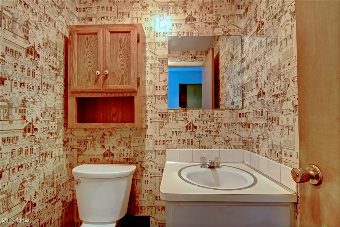 Half bath featuring vanity, toilet, and wallpapered walls