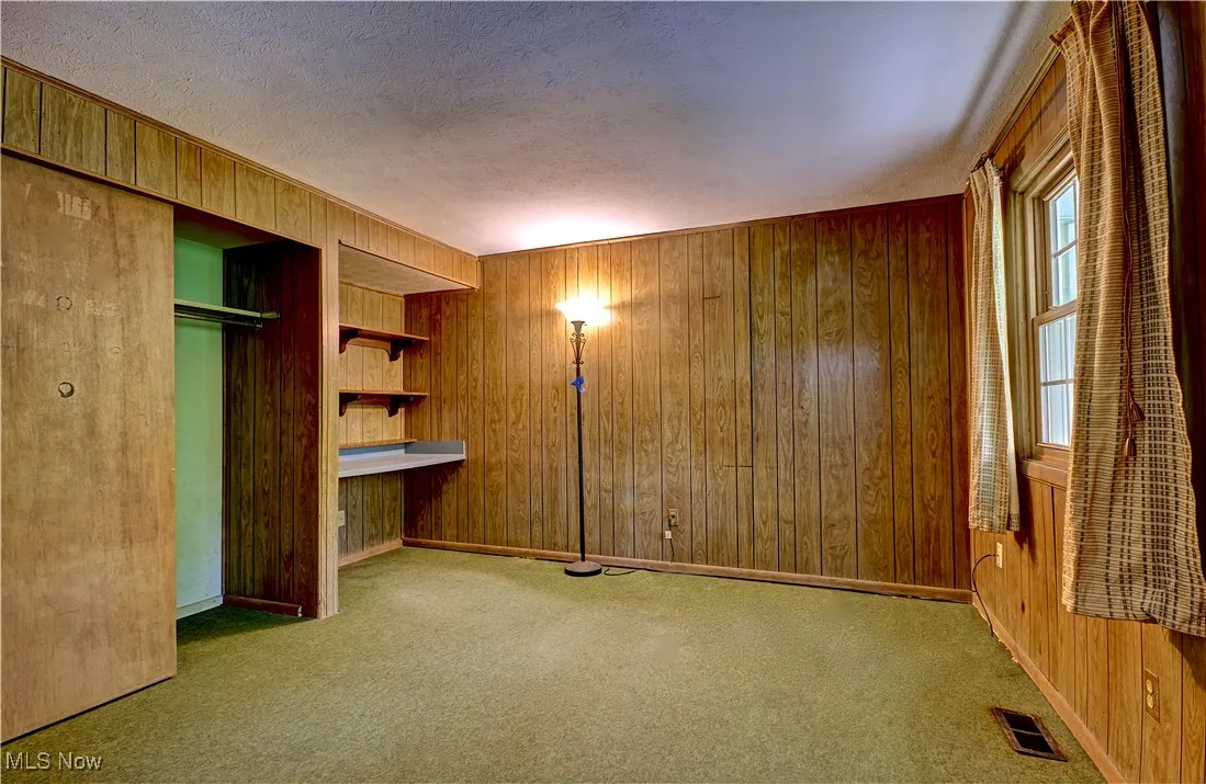 Unfurnished bedroom with wooden walls, carpet, a textured ceiling, and a closet