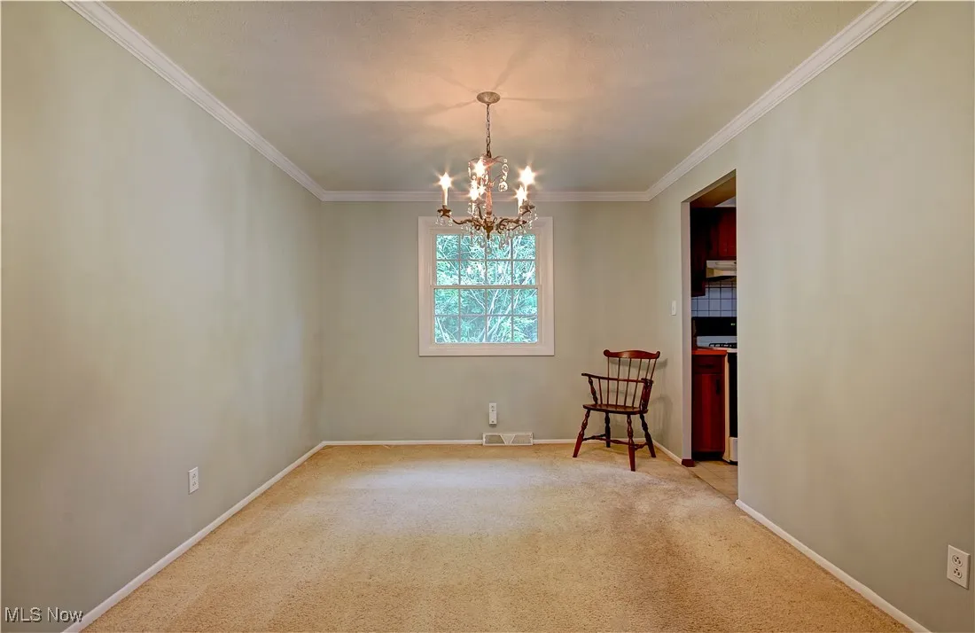 Carpeted empty room with a chandelier, ornamental molding, and baseboards