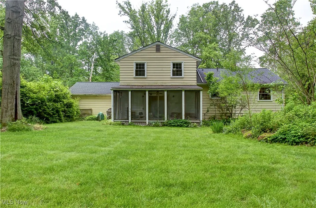 Rear view of house featuring a shingled roof, a sunroom, and a yard