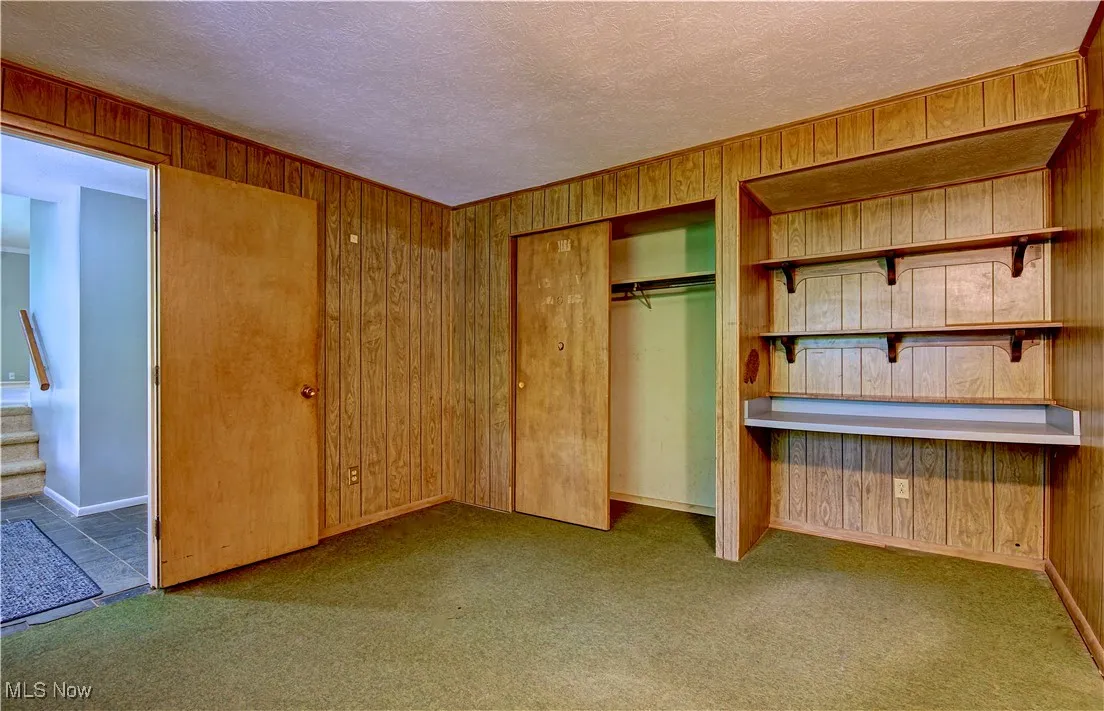 Unfurnished bedroom with wood walls, carpet floors, a textured ceiling, and a closet