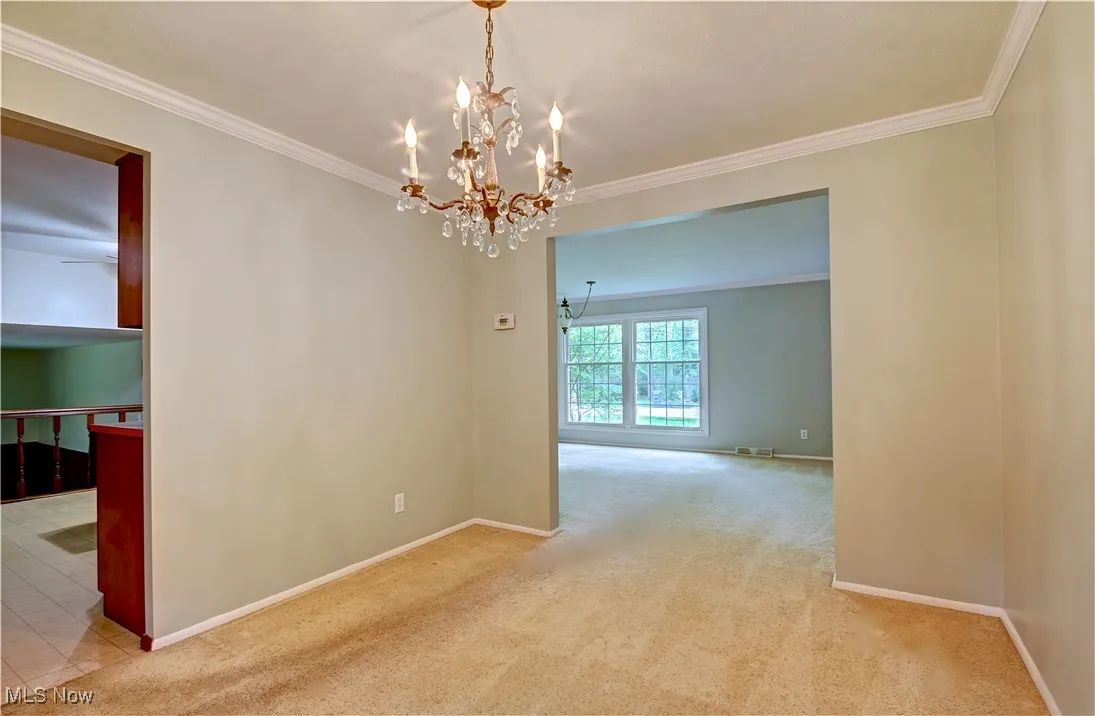 Carpeted spare room featuring a chandelier, ornamental molding, and baseboards