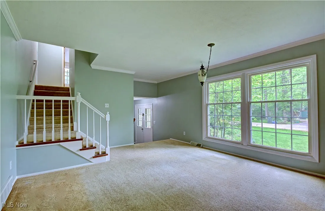Unfurnished living room with carpet, stairway, ornamental molding, and baseboards