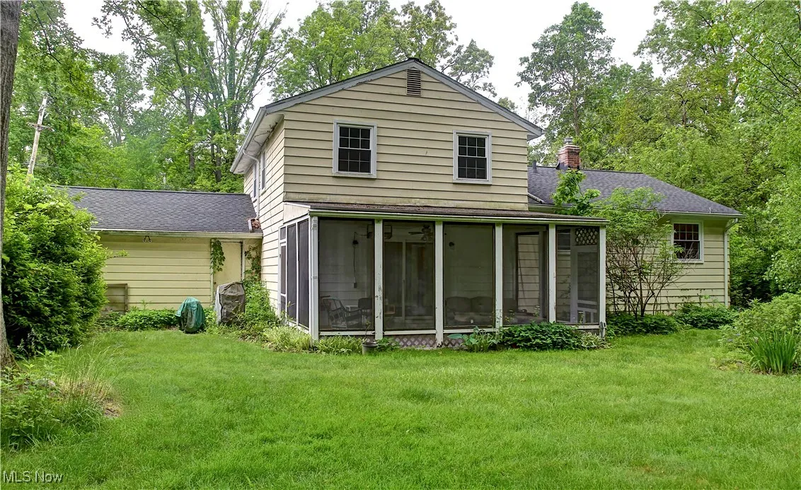 Rear view of property with a sunroom, a chimney, a lawn, and a shingled roof
