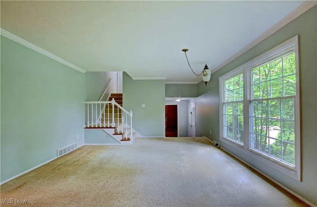 Unfurnished living room with stairway, crown molding, carpet, and baseboards