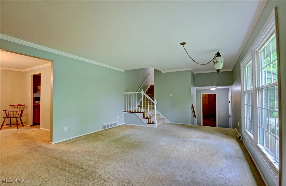 Empty room with stairs, ornamental molding, carpet flooring, and baseboards