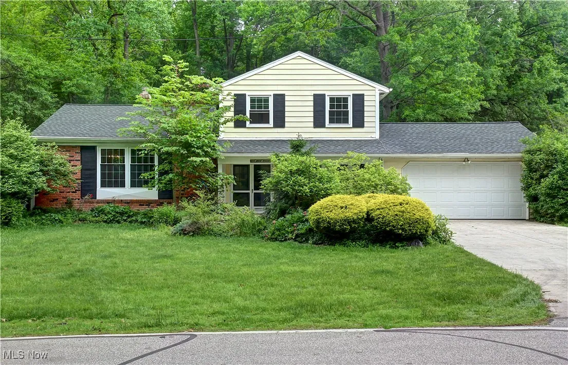 View of front of house with driveway, an attached garage, roof with shingles, a front lawn, and brick siding