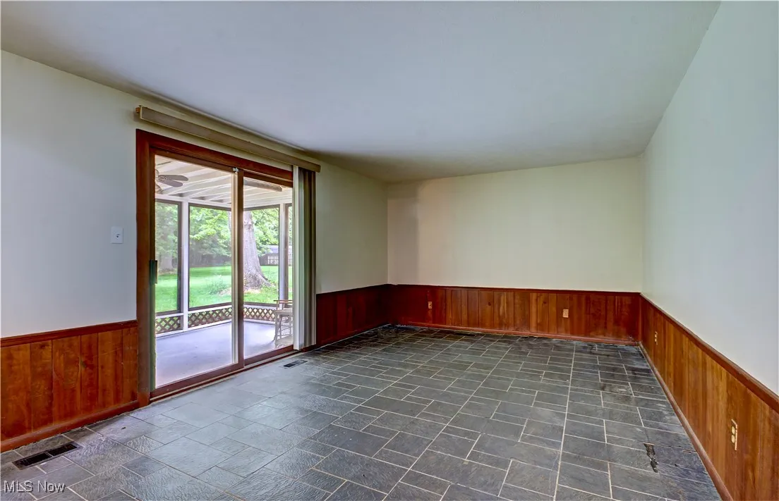 Spare room featuring a wainscoted wall, wood walls, and dark stone finish flooring