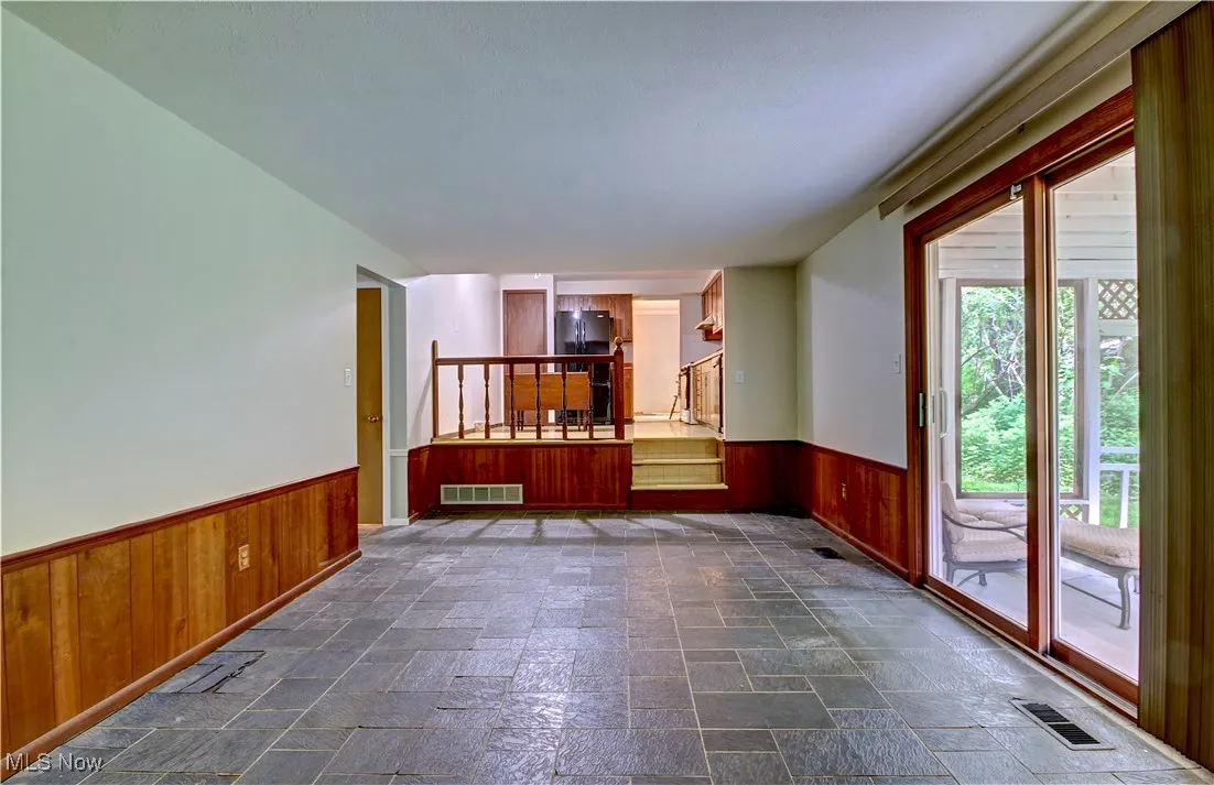 Unfurnished room with wainscoting, wooden walls, stone tile flooring, and stairs