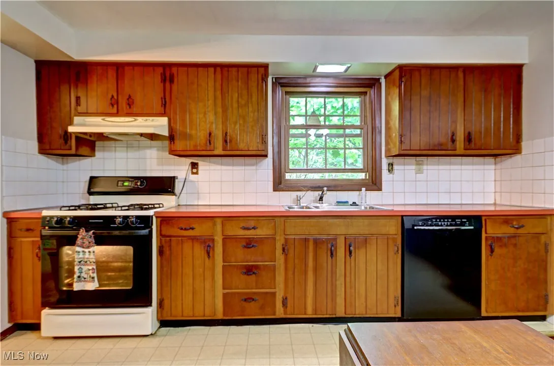 Kitchen with dishwasher, gas range oven, under cabinet range hood, a sink, and light countertops