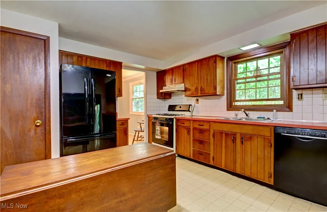 Kitchen featuring black appliances, a sink, under cabinet range hood, and plenty of natural light