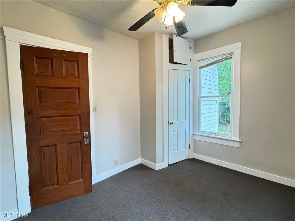 First floor bedroom featuring dark colored carpet, a textured ceiling, baseboards, and ceiling fan
