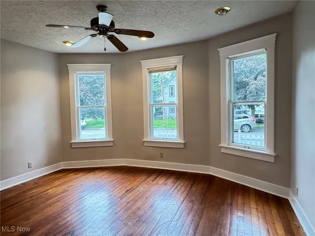 First floor room featuring dark wood finished floors, baseboards, ceiling fan, and a textured ceiling