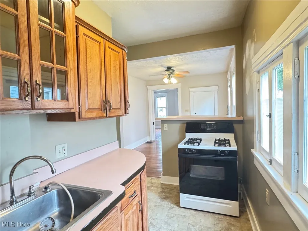 First floor Kitchen featuring range with gas stovetop, a sink, brown cabinetry, a ceiling fan, and glass insert cabinets