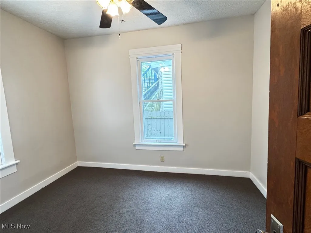 First floor bedroomwith dark carpet, ceiling fan, baseboards, and a textured ceiling