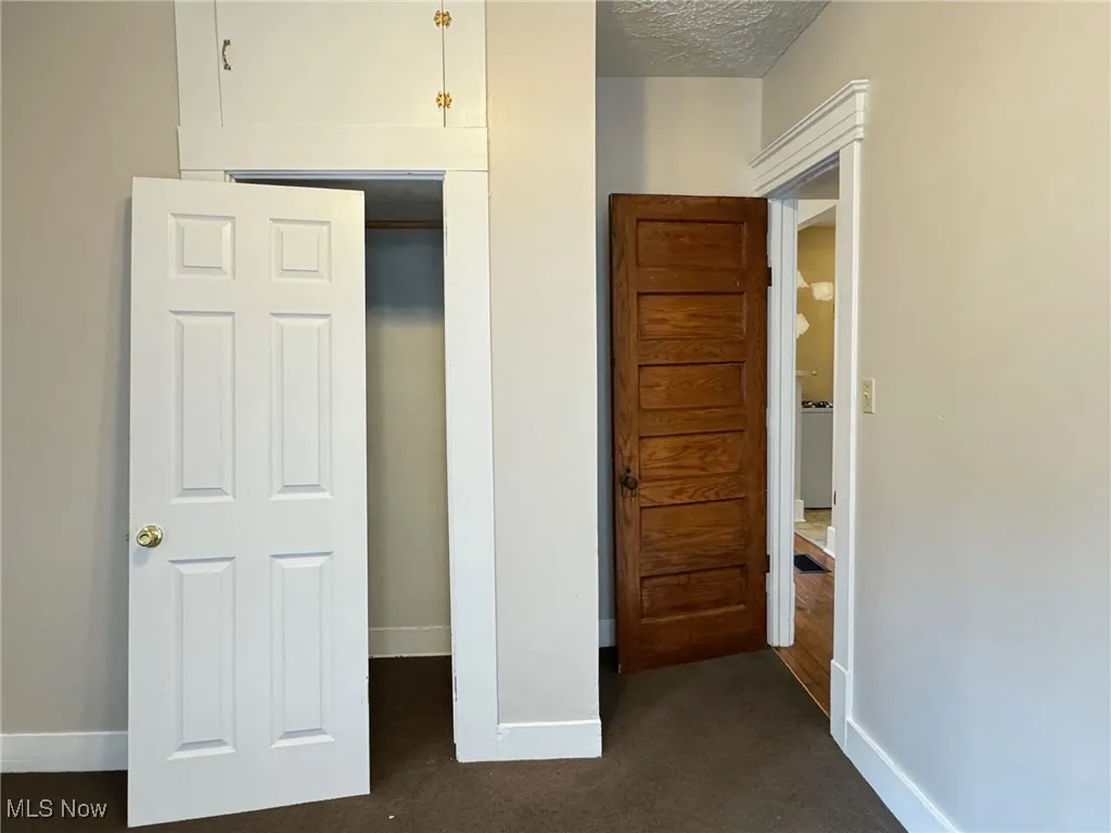 First floor bedroom with dark colored carpet, baseboards, and a textured ceiling
