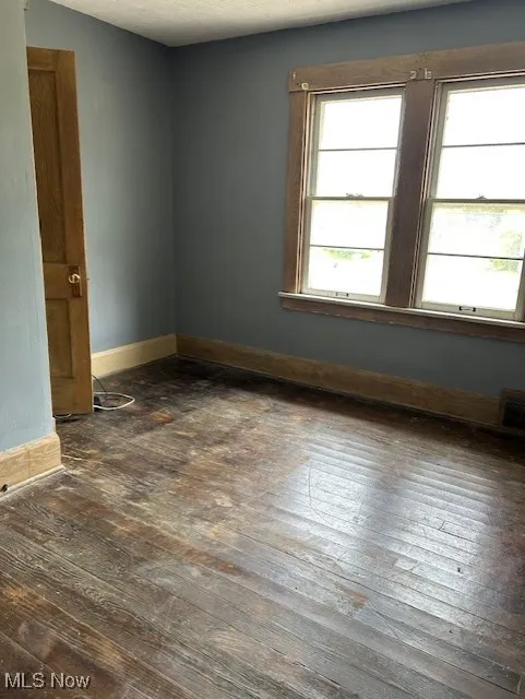 Empty room featuring dark wood-style floors and baseboards