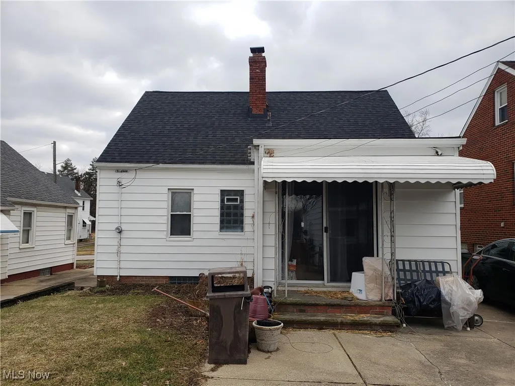 Back of property with a chimney and a shingled roof