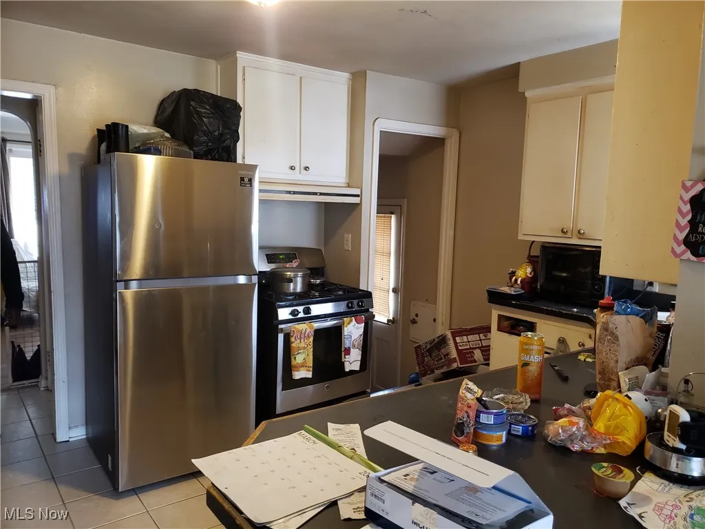 Kitchen featuring stainless steel appliances, under cabinet range hood, light tile patterned floors, white cabinets, and dark countertops