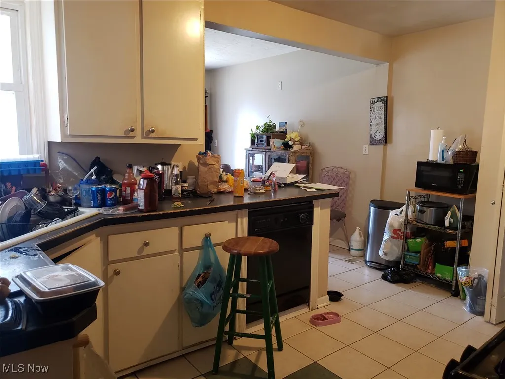 Kitchen featuring black appliances, light tile patterned flooring, dark countertops, and a breakfast bar