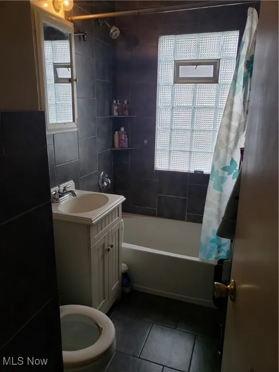 Full bath with tile patterned flooring, shower / bath combination with curtain, vanity, tile walls, and toilet