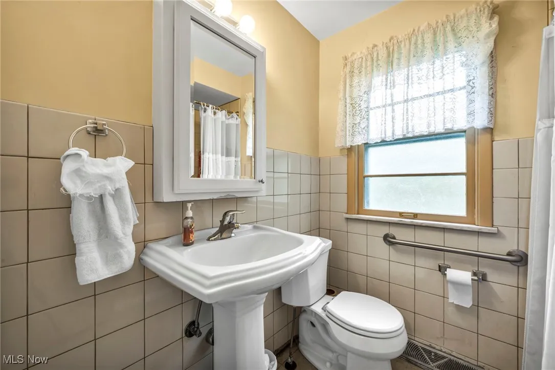Full bath with tile walls, toilet, a wainscoted wall, and a shower with curtain