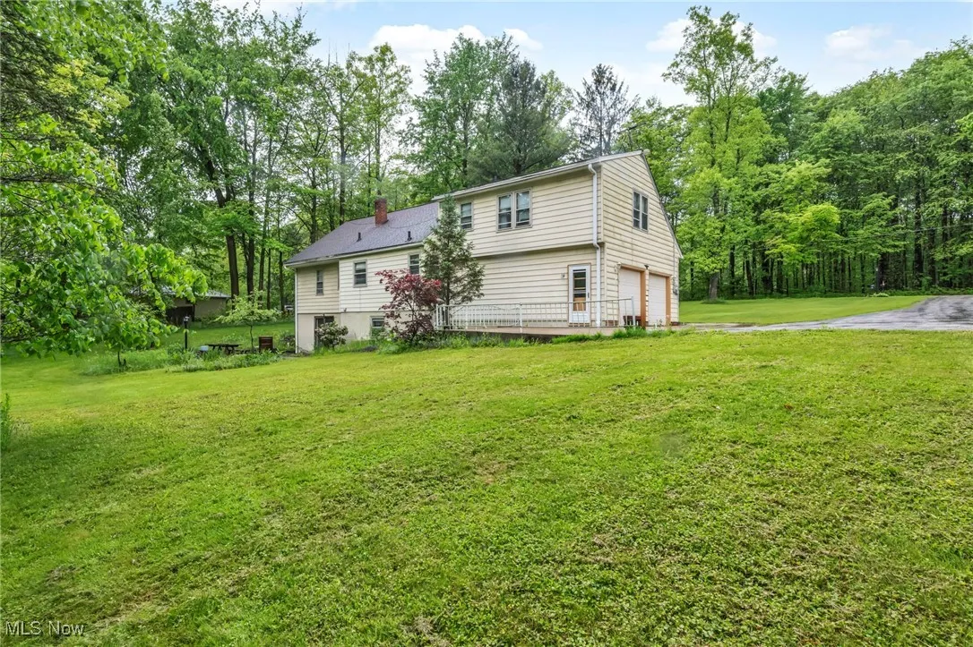 Back of property featuring a garage, a chimney, a yard, and driveway
