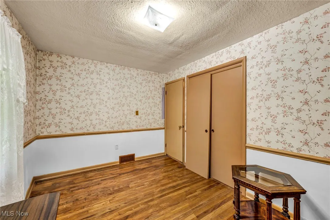 Unfurnished bedroom featuring wallpapered walls, light wood-style floors, a textured ceiling, and a closet