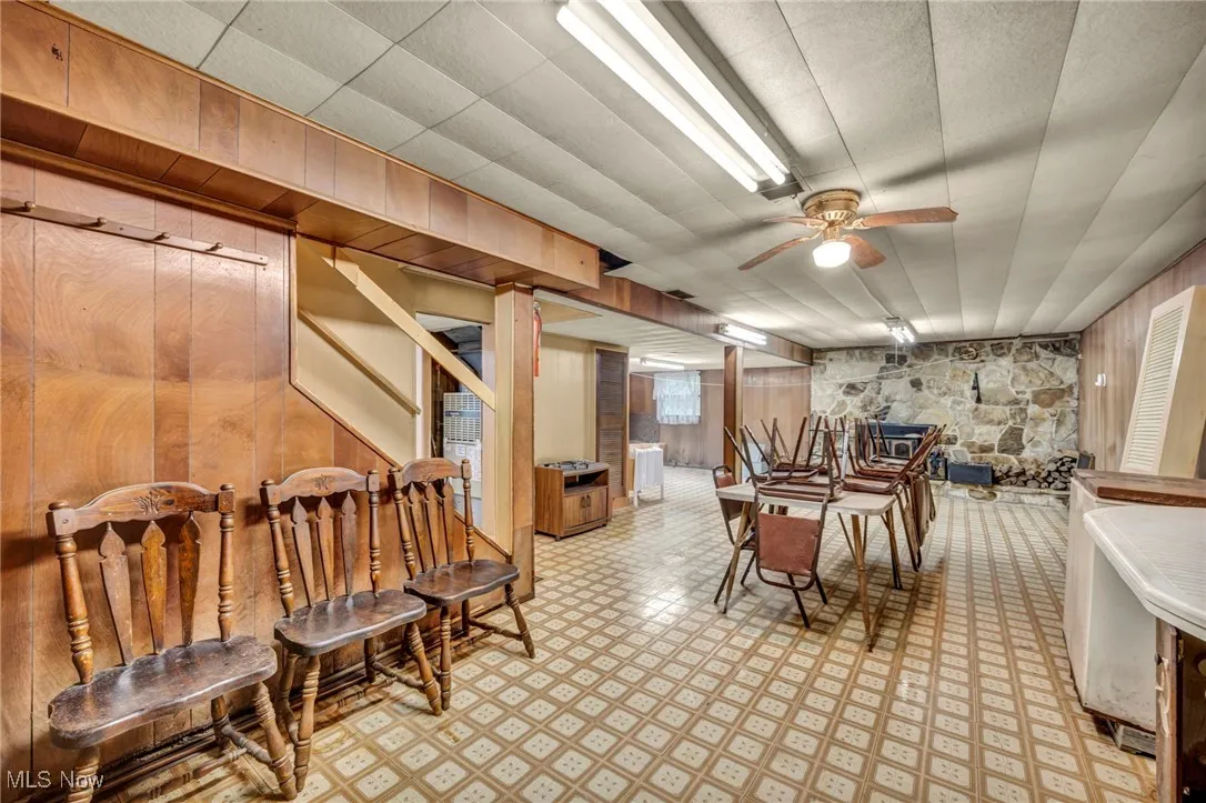 Dining space featuring wood walls, light floors, ceiling fan, and stairway