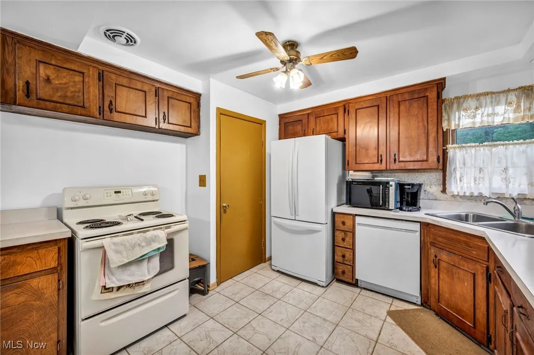 Kitchen featuring white appliances, a sink, a ceiling fan, and brown cabinets